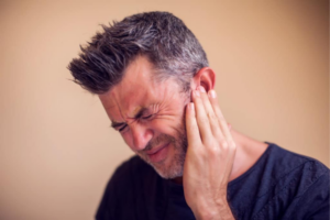 Man grimacing in pain while cupping his ear with his hand against a neutral background