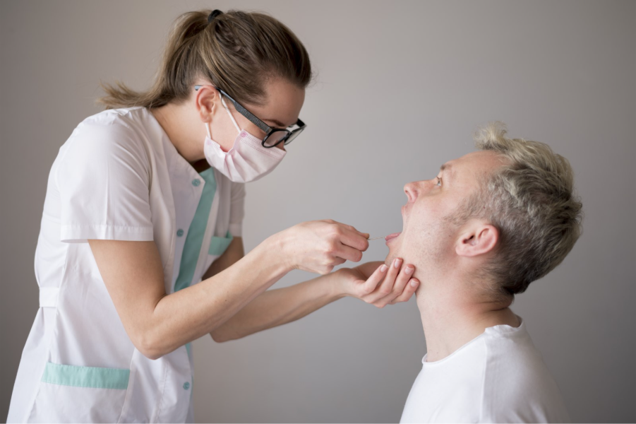 Nurse wearing a mask and glasses swabs a man's throat for a medical test in a clinical setting.