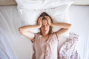 Woman experiencing sleep disruption while lying awake and distressed in bed.
