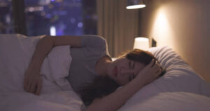 Woman experiencing the Effects of Sleep Deprivation while resting uncomfortably in bed.