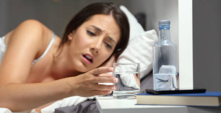 Woman waking up with a dry mouth while sleeping, reaching for a glass of water on the nightstand